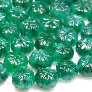 May include: A collection of green emerald gemstone beads with a faceted, carved design. The beads are round and have a smooth, polished finish.