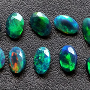Puede incluir: Una colección de diez ópalos ovalados con corte facetado. Los ópalos muestran una gama de colores, incluyendo azules profundos, verdes vibrantes y destellos de naranja y amarillo. Las piedras preciosas están dispuestas sobre una superficie texturizada de color gris oscuro.