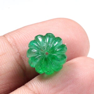 May include: A green emerald gemstone carved into a flower shape. The gemstone has a hole drilled through the center.