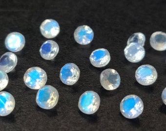 May include: A collection of iridescent white moonstone gemstones, each with a unique, faceted shape. The stones are arranged on a black surface, showcasing their shimmering, opalescent qualities.