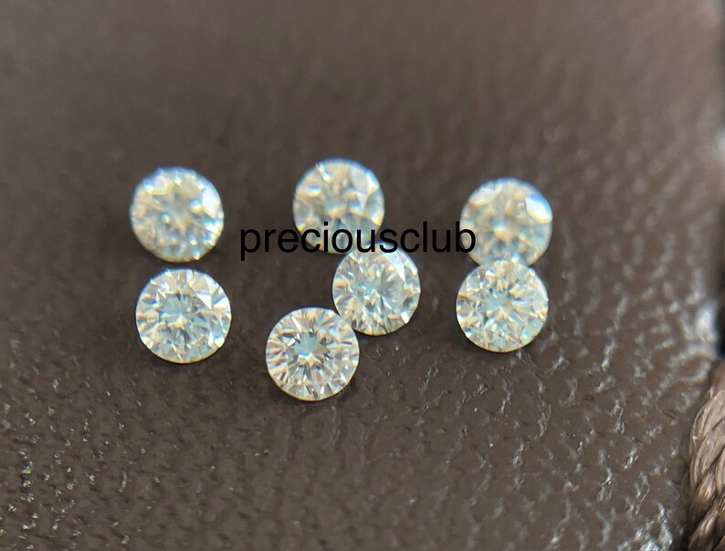 Pode incluir: Sete pedras preciosas redondas, transparentes e facetadas sobre uma superf&iacute;cie marrom texturizada. preciousclub est&aacute; escrito em branco na superf&iacute;cie.