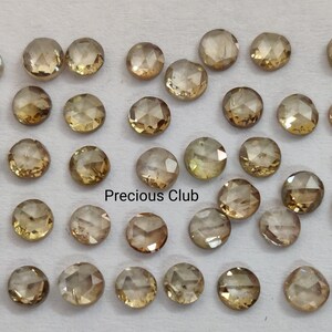 以下が含まれることがあります： 36個のばら売りの茶色のダイヤモンドの集合。それぞれがファセットカットされた丸い形をしています。ダイヤモンドは白い表面にランダムなパターンで配置されています。画像の下中央には「Precious Club」というテキストが表示されています。