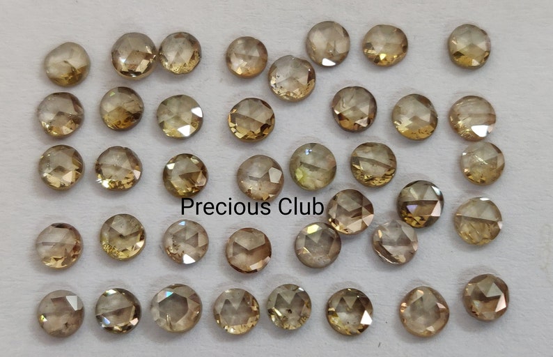 May include: A collection of 40 round, faceted, brown diamonds. The diamonds are loose and arranged in rows on a white surface. The text "Precious Club" is visible in the center of the image.