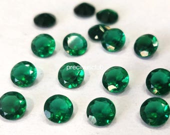 May include: A collection of round, faceted emerald green gemstones arranged in a scattered pattern. Each stone features a brilliant cut with multiple reflective surfaces. The text "preciousclub" is printed in small white letters in the center.