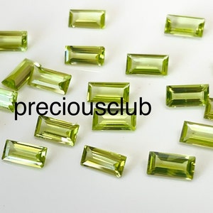 May include: A collection of 15 green peridot gemstones cut in a rectangular shape. The gemstones are arranged on a white surface. preciousclub is printed in black text on the surface.