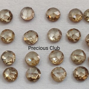 May include: Twenty-four round, faceted, brown diamonds arranged in four rows of six. The diamonds are set on a white background. The text "Precious Club" is printed in black below the diamonds.