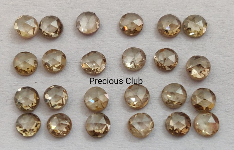 May include: Twenty-four round, faceted, brown diamonds arranged in four rows of six. The diamonds are set on a white background. The text "Precious Club" is printed in black below the diamonds.