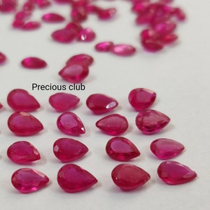 Può includere: Una collezione di pietre preziose a forma di pera, di colore rosa intenso. Le pietre preziose sono disposte in file su una superficie bianca. Il testo "Precious club" è visibile nell'immagine.