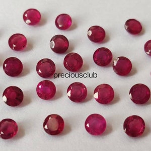 May include: A collection of small, round, faceted red rubies scattered across a white surface. Each gemstone displays a brilliant crimson hue with multiple facets reflecting light. The text "preciousclub" is printed in black in the center.