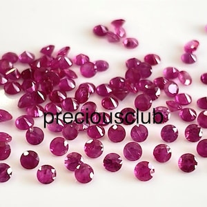 Puede incluir: Una colección de numerosas piedras preciosas pequeñas, redondas y facetadas de color magenta esparcidas sobre una superficie blanca. El texto "preciousclub" está impreso en negro en el centro de la disposición de estas piedras pulidas.