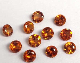 May include: A collection of faceted, round and oval-shaped gemstones. The gems are a warm, amber-orange color, with brilliant internal reflections. The gemstones are scattered across a white surface, showcasing their clarity and cut. Ideal for jewelry making.