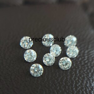 Pode incluir: Um grupo de dez pequenos diamantes redondos e transparentes sobre uma superf&iacute;cie preta. Os diamantes s&atilde;o todos do mesmo tamanho e t&ecirc;m um corte brilhante.