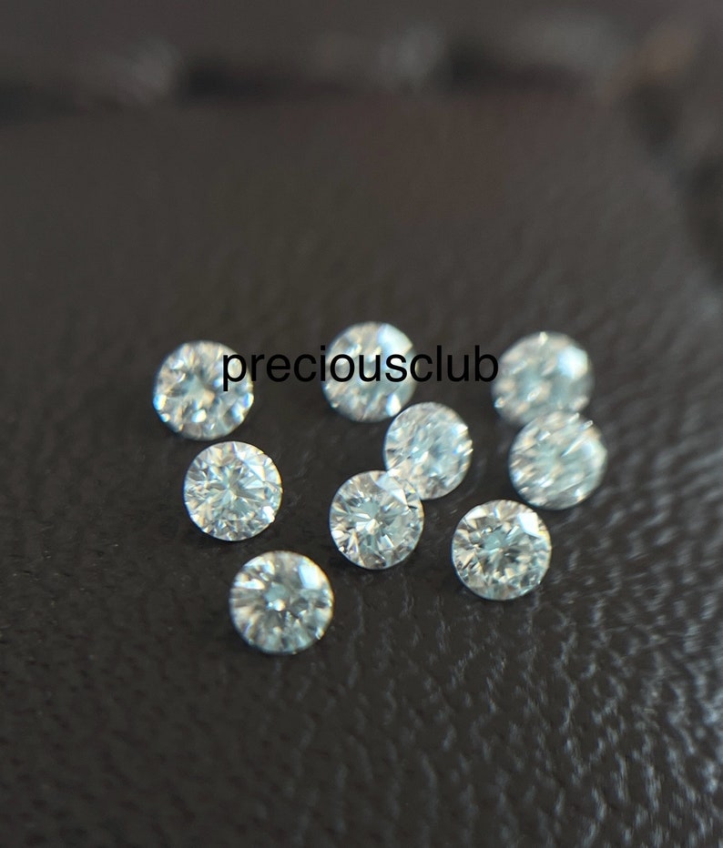 Pode incluir: Um grupo de dez pequenos diamantes redondos e transparentes sobre uma superf&iacute;cie preta. Os diamantes s&atilde;o todos do mesmo tamanho e t&ecirc;m um corte brilhante.