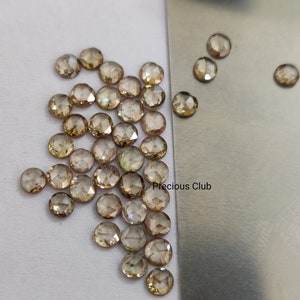 以下が含まれることがあります： 丸みを帯びたファセットカットの茶色のダイヤモンドの集合。ローズカットダイヤモンドとしても知られています。ダイヤモンドは白い表面と銀色の表面に散らばっており、"Precious Club"という文字が書かれています。