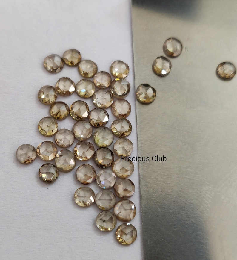 以下が含まれることがあります： 丸みを帯びたファセットカットの茶色のダイヤモンドの集合。ローズカットダイヤモンドとしても知られています。ダイヤモンドは白い表面と銀色の表面に散らばっており、"Precious Club"という文字が書かれています。