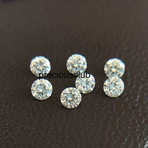 Pode incluir: Sete pedras preciosas redondas, transparentes e facetadas sobre uma superf&iacute;cie marrom escura. As pedras preciosas s&atilde;o pequenas e parecem ser diamantes.