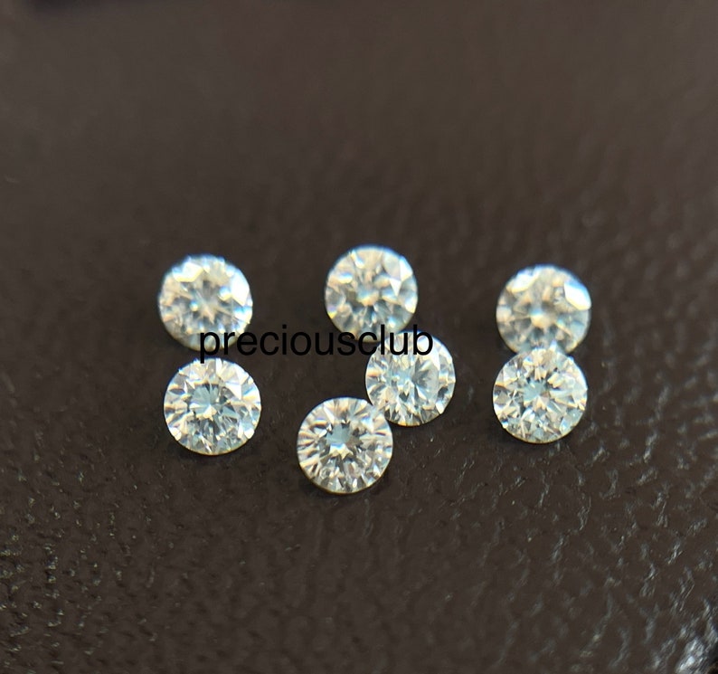 Pode incluir: Sete pedras preciosas redondas, transparentes e facetadas sobre uma superf&iacute;cie marrom escura. As pedras preciosas s&atilde;o pequenas e parecem ser diamantes.