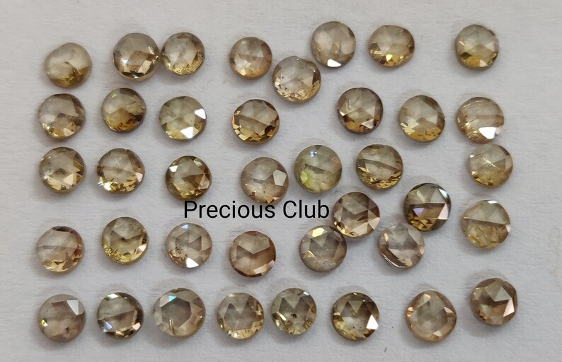 May include: A collection of 40 round, faceted, brown diamonds. The diamonds are loose and scattered on a white surface. The text "Precious Club" is visible in the center of the image.