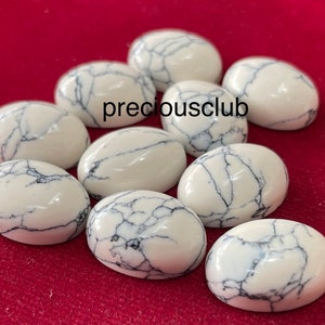 May include: Nine white oval cabochon stones with black veining. The stones are arranged in a circle on a red surface. The text "preciousclub" is visible in the center of the image.