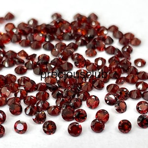 Puede incluir: Un montón de piedras preciosas redondas rojas sueltas. Las piedras preciosas están esparcidas sobre una superficie blanca. El texto "preciousclub" es visible en la imagen.