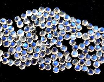 May include: A collection of round, iridescent moonstone cabochons in various shades of white and blue. The stones are scattered on a black surface.