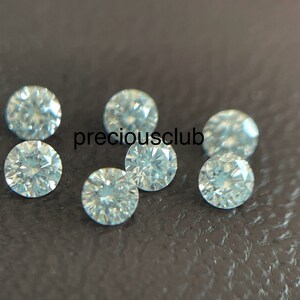 Pode incluir: Sete pedras preciosas redondas e facetadas transparentes, provavelmente diamantes, sobre uma superf&iacute;cie texturizada cinza escura. As pedras preciosas est&atilde;o espalhadas aleatoriamente.