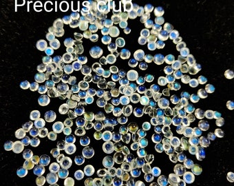 May include: A collection of iridescent moonstone cabochons in various sizes, scattered on a black background. The stones have a milky white base with blue and green iridescent flashes.