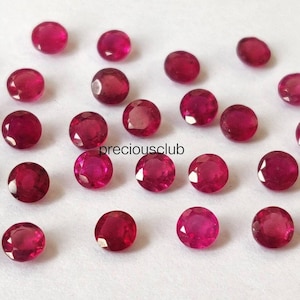 Peut inclure: Une collection de petites pierres précieuses rouges, rondes et facettées, disposées de manière éparse. Chaque pierre présente une taille brillant avec de multiples surfaces réfléchissantes. Le texte "preciousclub" est imprimé en noir au centre.