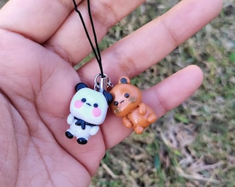 May include: A black string phone charm with a white panda bear and a brown bear charm. The panda bear has black eyes and a pink nose. The brown bear has brown eyes and a pink nose.