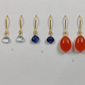 Könnte beinhalten: Drei Paar goldene Ohrringe mit verschiedenen Edelsteinen. Das erste Paar hat hellblaue Edelsteine, das zweite Paar hat dunkelblaue Edelsteine und das dritte Paar hat orangefarbene Edelsteine.