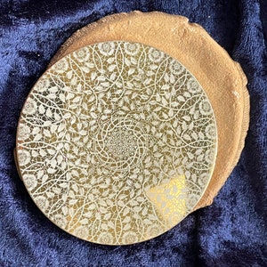 Può includere: Un compatto dorato con un design a pizzo bianco. Il compatto è chiuso e ha una forma rotonda.