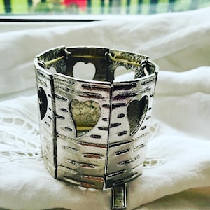 Puede incluir: Pulsera de plata con diseño de corteza de abedul y recortes en forma de corazón. La pulsera está marcada con el número "22 B01".