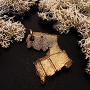 Könnte beinhalten: Ein goldfarbener Metallanhänger mit einem einzigartigen, gebrochenen und strukturierten Design. Der Anhänger hat oben einen kleinen Ring zum Anbringen einer Kette.