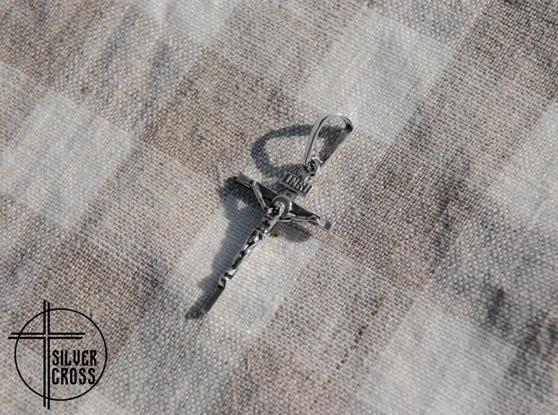 Pode incluir: Um pingente de prata em forma de crucifixo com um design detalhado. O pingente tem um la&ccedil;o na parte superior para prender a uma corrente.