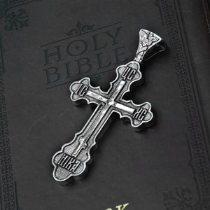May include: A silver cross pendant with intricate details and Cyrillic lettering. The cross is lying on a black leather-bound Holy Bible.