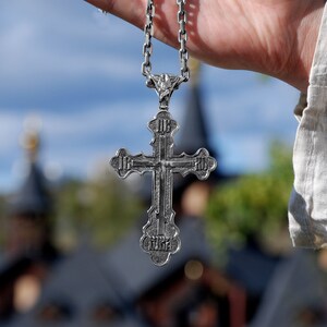 May include: A silver cross pendant with intricate details hangs from a silver chain. The cross is a religious symbol and is often worn as a necklace.