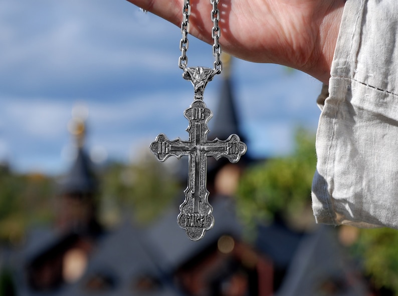May include: A silver cross pendant with intricate details hangs from a silver chain. The cross is a religious symbol and is often worn as a necklace.