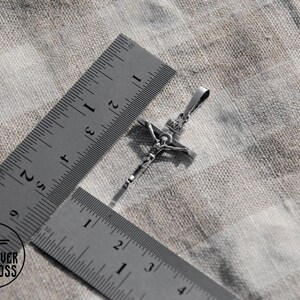 Pode incluir: Um pingente de prata em forma de crucifixo com uma figura detalhada de Jesus Cristo. O pingente &eacute; medido com uma r&eacute;gua, mostrando que tem aproximadamente 5 cm de comprimento.