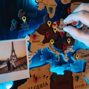 A hand is placing a small object on a map of Europe, which is decorated with various country shapes and labels.