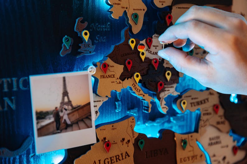 A hand is placing a small object on a map of Europe, which is decorated with various country shapes and labels.