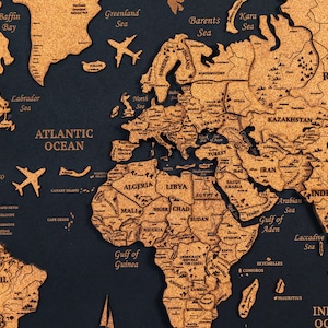 以下が含まれることがあります： コルクで作られた詳細な世界地図で、国と海がラベル付けされています。 地図は濃い青色の背景と明るい茶色のコルクの表面が特徴です。 飛行機の切り抜きが地図全体に配置されています。