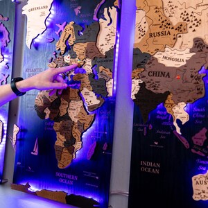 a person pointing at a wooden world map with illuminated labels, creating a visually striking and engaging display.
