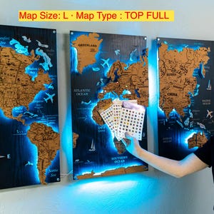 A man is holding a small set of cards in front of a wall with three large world map posters.