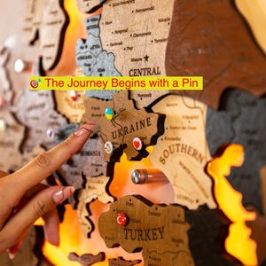 A hand is pointing at a wooden map of Europe, with the word "TURKEY" visible on one of the map pieces.
