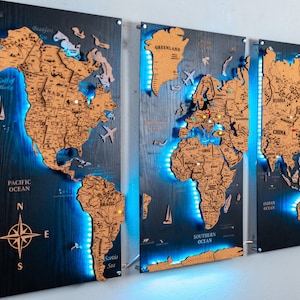 May include: A three-panel wooden world map wall art piece featuring laser-cut continents in a natural wood finish mounted on dark, textured black boards. The display is illuminated by blue LED backlighting and includes a compass rose.