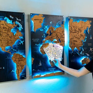 A man is holding a small set of cards in front of a wall with three large world map posters.