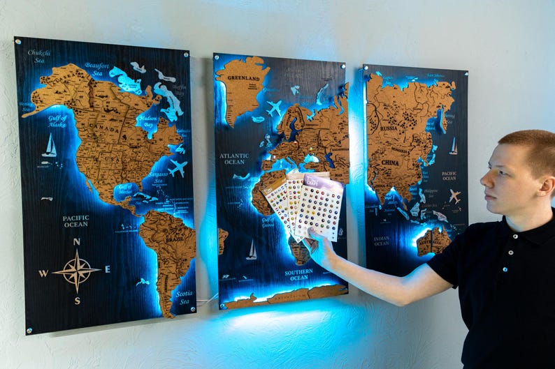 A man is holding a small set of cards in front of a wall with three large world map posters.