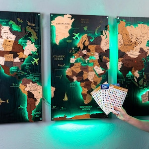 A man is standing in front of three large, illuminated world map posters on a wall, holding some stickers.