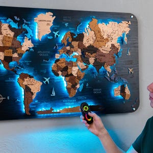 A person is holding a remote control in front of a large world map that is illuminated with blue lights, creating a visually striking and unique display.