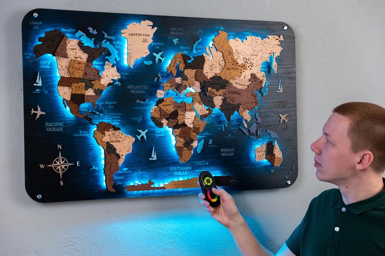 A person is holding a remote control in front of a large world map that is illuminated with blue lights, creating a visually striking and unique display.